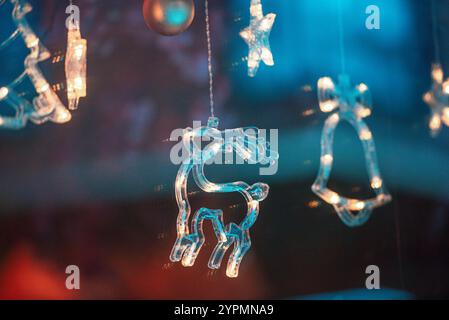 Zauberhafte Weihnachtsszene mit Blauhirsch, Glocke und baumförmigen Ornamenten, die vor Funkeln leuchten. Die bunten Lichter, die sich im Fenster spiegeln Stockfoto