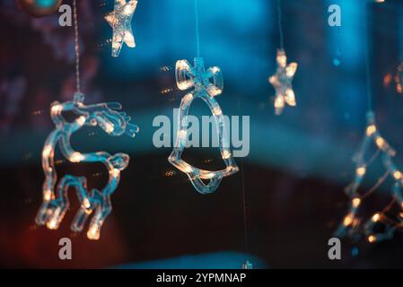 Zauberhafte Weihnachtsszene mit Blauhirsch, Glocke und baumförmigen Ornamenten, die vor Funkeln leuchten. Die bunten Lichter, die sich im Fenster spiegeln Stockfoto