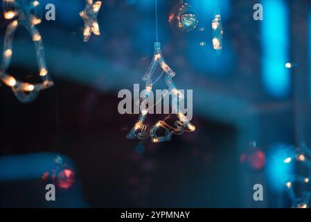 Zauberhafte Weihnachtsszene mit Blauhirsch, Glocke und baumförmigen Ornamenten, die vor Funkeln leuchten. Die bunten Lichter, die sich im Fenster spiegeln Stockfoto