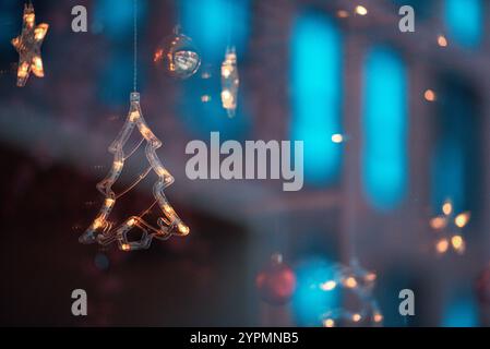 Zauberhafte Weihnachtsszene mit Blauhirsch, Glocke und baumförmigen Ornamenten, die vor Funkeln leuchten. Die bunten Lichter, die sich im Fenster spiegeln Stockfoto