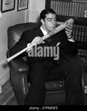 Joe DiMaggio, Mittelfeldspieler bei den New York Yankees, trägt einen Anzug, sitzt auf einem Stuhl und grüßt seinen Baseballschläger mit einem Kuss. Dezember Stockfoto