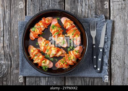 Uunimakkara, gebacken im Ofen Würstchen mit Käse, Tomaten und Senf in Backform auf grauem Holztisch mit Besteck, finnisches Retro-Rezept, Hor Stockfoto