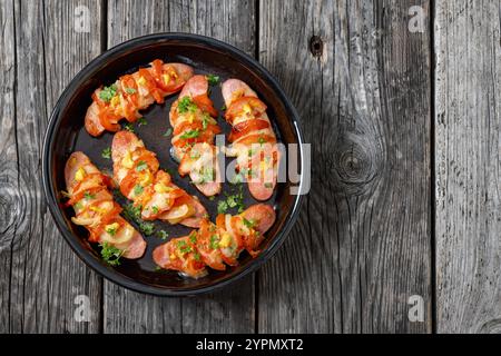 Uunimakkara, gebacken im Ofen Würstchen mit Käse, Tomaten und Senf in Backform auf grauem rustikalem Holztisch, finnisches Retro-Rezept, horizonta Stockfoto