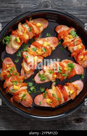 Uunimakkara, gebacken im Ofen Würstchen mit Käse, Tomaten, Petersilie, Senf in Backform auf grauem rustikalem Holztisch, finnisches Retro-Rezept, ver Stockfoto