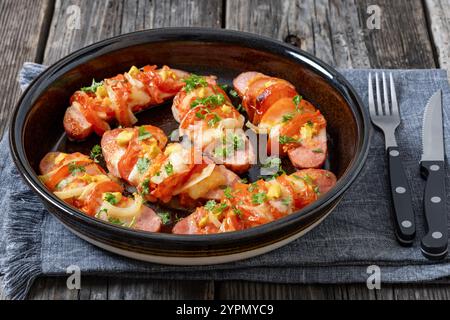 Uunimakkara, gebacken im Ofen Würstchen mit Käse, Tomaten und Senf in Backform auf grauem Holztisch mit Besteck, finnisches Retro-Rezept, Clo Stockfoto