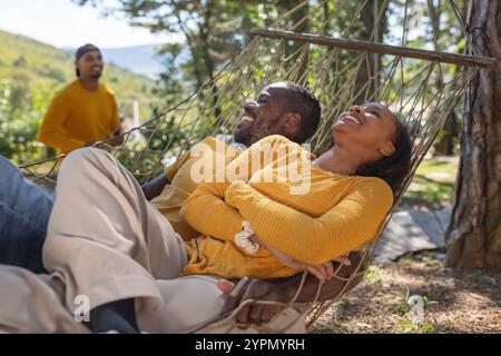 Sorglos lächelnde afroamerikanische Freunde verbringen ihren Urlaubstag in einer Hängematte und genießen eine wunderschöne Glamping-Umgebung. Stockfoto