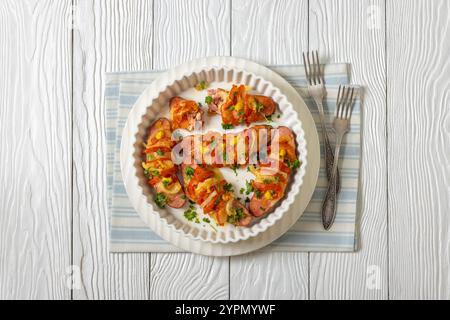 Uunimakkara, gebacken im Ofen Würstchen mit Käse, Tomaten, Senf in Backform auf weißem Holztisch mit Gabeln, finnisches klassisches Rezept, horiz Stockfoto