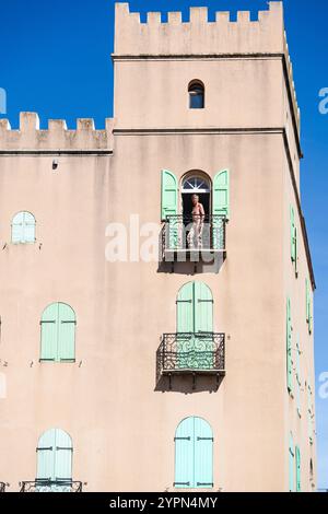 Ein älterer Mann mit offenem Oberkörper auf dem Balkon eines Hauses mit grünen Fensterläden im historischen Zentrum von Collioure, Frankreich Stockfoto