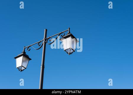 Ein Laternenpfahl mit zwei Laternen isoliert vor einem blauen Himmel Stockfoto