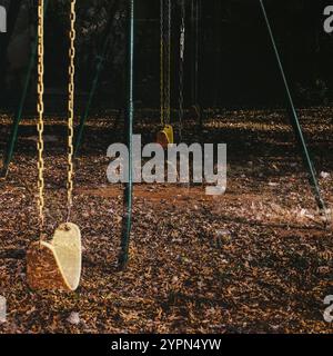 Leere Schaukeln hängen still auf einem Spielplatz, umgeben von heruntergefallenen Blättern, die den Boden bedecken. Stockfoto