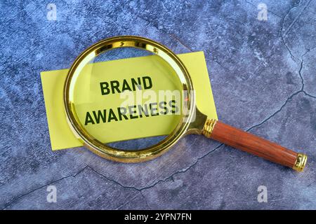 Geschäftskonzept. Worte ZUR MARKENBEKANNTHEIT, die durch eine Lupe geschrieben werden, Draufsicht auf gelbem Papier. Stockfoto