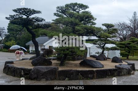 Japan, Himeji Castle. Große Felsen und schwarze Kiefern am Eingang, zwei Frauen in traditioneller Kimono-Kleidung, regnerischer Tag Stockfoto