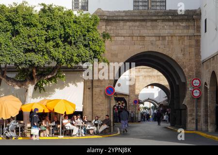 Das große Habous-Tor mit einem Steinbogen und die Leute sitzen in einem Café im Freien mit gelben Sonnenschirmen. Das Hotel liegt in Casablanca, Marokko, Habous Stockfoto