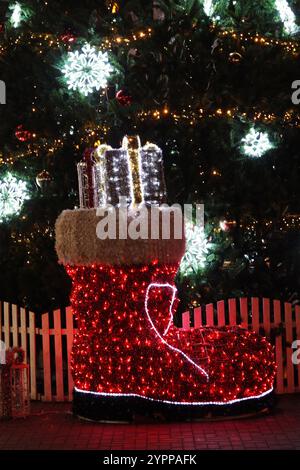 Großer dekorativer Weihnachtsmann-Stiefel mit Girlanden auf dem Hintergrund eines Weihnachtsbaumes, Neujahrsbaum. Festliche Dekoration, Beleuchtung. Stockfoto
