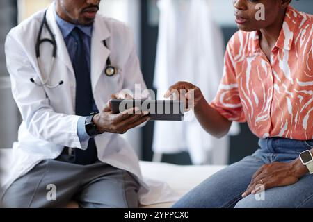 Zugeschnittene Aufnahme einer jungen Frau als Patientin, die auf den Tablet-Bildschirm zeigt und während der Sprechstunde Fragen an den Arzt mit Laborkittel stellt Stockfoto