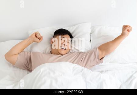 Draufsicht eines lächelnden Asiaten, der sich im Bett streckt Stockfoto