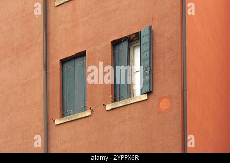 Verwitterte orangefarbene Wand mit blauen Fensterläden Stockfoto