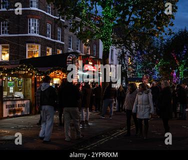 Die Menschenmassen versammeln sich am Abend auf einem Weihnachtsmarkt mit beleuchteten Bäumen und dekorierten Ständen in einer gemütlichen urbanen Umgebung. York Christmas Market 2024 Stockfoto