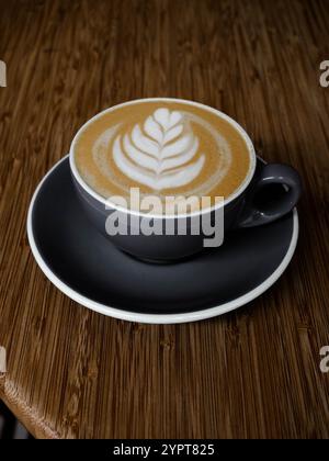 Nahaufnahme eines Cappuccinos mit schönem Schaum in einer grauen Tasse auf einem Holztisch - warme und stilvolle Kaffeezubereitung Stockfoto