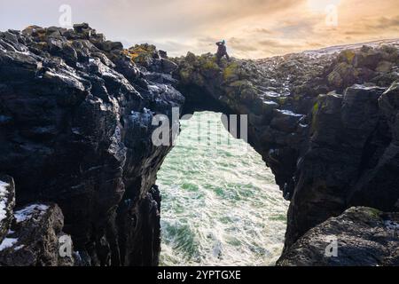 Blick auf einen Fotografen, der auf der Steinbrücke steht. Arnarstapi, Halbinsel Snæfellsnes, Island, Nordeuropa. Stockfoto