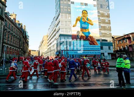 Die Teilnehmer laufen während des Liverpool Santa Dash 2024 an einem Wandgemälde vorbei. Die Teilnehmer trafen in roten (und blauen) Santa Suits auf einer 5 km langen Strecke durch das Stadtzentrum von Liverpool, um das Claire House Kinderhospiz zu unterstützen. 8.500 Teilnehmer nahmen am 20. Jährlichen Liverpool Santa Dash Teil. Stockfoto