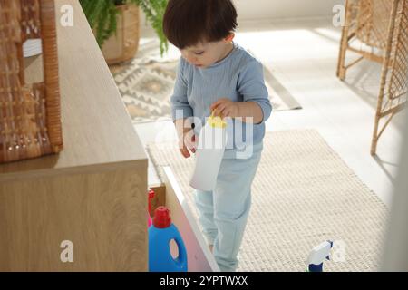 Kleiner Junge, der mit Waschmittelflaschen in der Nähe des Schranks zu Hause spielt. Kind in Gefahr Stockfoto