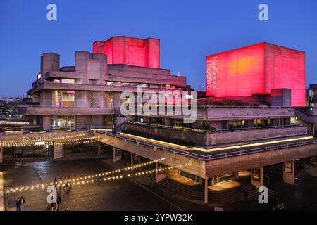 London, Großbritannien. Dezember 2024. Das Nationaltheater ist teilweise rot beleuchtet, was ihm einen festlichen saisonalen Look verleiht. Nach einem Tag mit starken Schauern und milden Temperaturen sieht der erste Tag im Dezember klaren Himmel bei Sonnenuntergang. Quelle: Imageplotter/Alamy Live News Stockfoto