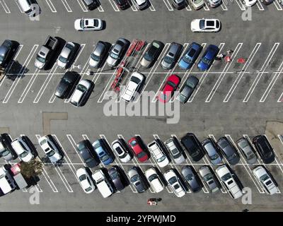 Blick von oben auf den Parkplatz im Einkaufszentrum mit verschiedenen farbigen Fahrzeugen. Leute, die zu ihrem Auto gehen und versuchen zu parken Stockfoto