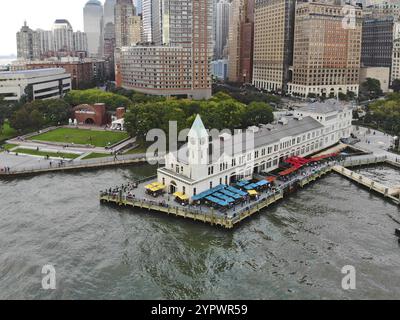 Aus der Vogelperspektive des Battery Park Pier A, der nach Liberty Island führt, kann man Menschen sehen, die in der Schlange stehen, um an Bord zu gehen, und auf Liberty Island loc blicken Stockfoto