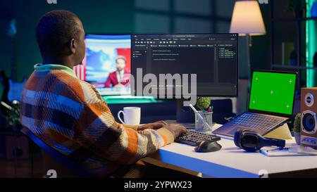 Schwarzer Webentwickler, der Datenbankserver für Sicherheit handhabt, mit grünem Bildschirm, der Code auf das Terminalfenster neben dem isolierten Chroma-Schlüssel schreibt. Programmiersprache für maschinelles Lernen. Kamera A.. Stockfoto