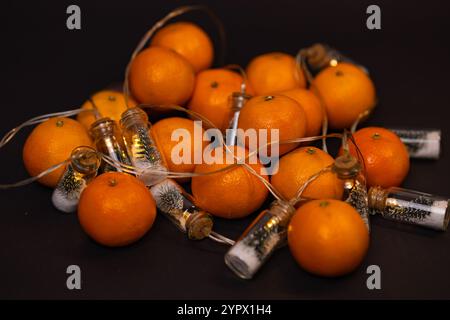 Festliche Anordnung frischer Mandarinen mit dekorativen Glasgläsern mit Miniatur-Weihnachtsbäumen und Schnee auf dunklem Hintergrund Stockfoto