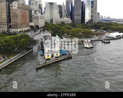 Aus der Vogelperspektive des Battery Park Pier A, der nach Liberty Island führt, kann man Menschen sehen, die in der Schlange stehen, um an Bord zu gehen, und auf Liberty Island loc blicken Stockfoto