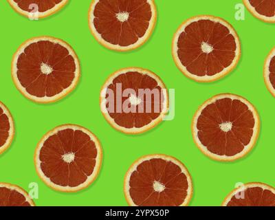 Kreatives Muster aus roten Orangen. Blick von oben auf farbenfrohes Fruchtmuster mit frischen roten orangen Scheiben auf grünem farbenfrohen Hintergrund Stockfoto