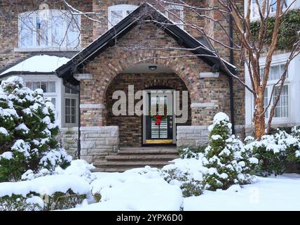 Haus mit schneebedeckten Büschen und bunten Weihnachtskranz an der Haustür Stockfoto