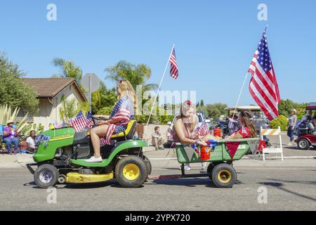 Junge Mädchen mit amerikanischer Flagge, die auf einem kleinen Rasenmäher reiten und bei der Parade zum Unabhängigkeitstag am 4. Juli in Rancho Bernardo, San Diego, Kalifornien, vormarschieren Stockfoto