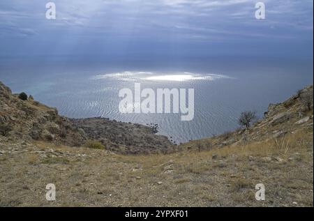 Die Sonnenstrahlen bahnen ihren Weg durch die Wolken und hinterlassen Lichtpunkte auf der Meeresoberfläche. Blick vom Gipfel des Cape Meganom. Krim, Wolkentag im Oktob Stockfoto