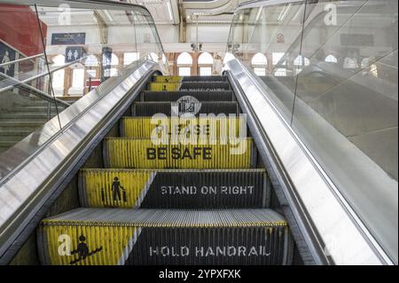Rolltreppe am Bahnhof mit Meldung zur Trittstufe. Bitte seien Sie sicher, stehen Sie rechts und halten Sie den Handlauf. Warnschild und Warnung Stockfoto