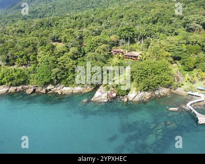 Blick aus der Vogelperspektive auf das luxuriöse Haus im tropischen Wald, umgeben von Bäumen und neben dem Meer und dem blauen türkisfarbenen Wasser. Luxuriöse Villa und geräumige Pavili Stockfoto