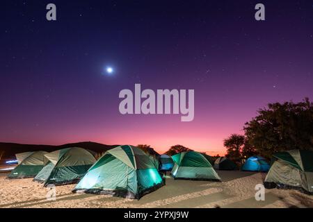 Ein Vollmond erleuchtete diese Szene am frühen Morgen einer Gruppe von Zelten auf einem Campingplatz im Süden Namibias. Stockfoto