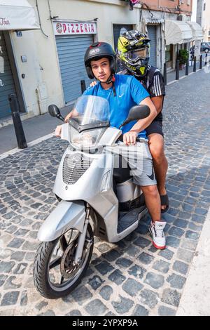 Civitavecchia Italien, in der Nähe der Via Colle dell'Olivo, Fahrer Silber Roller, Teenager mit Helmen, Passagierroller, städtische Straßenszene Kopfsteinpflaster, Pizzeria Stockfoto