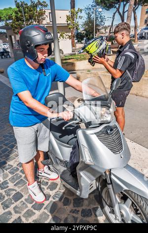 Civitavecchia Italien, in der Nähe der Via Colle dell'Olivo, Fahrer Silber Roller, Teenager mit Helmen, urbane Straßenszene, Kopfsteinpflasterstraße, Sicherheitsausrüstung, Helm Stockfoto