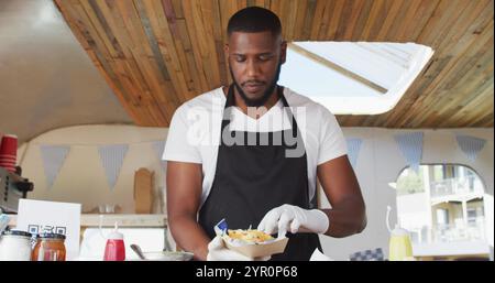 Porträt eines afroamerikanischen Mannes, der eine Schürze trägt und lächelt, während er im Food Truck Essen serviert Stockfoto