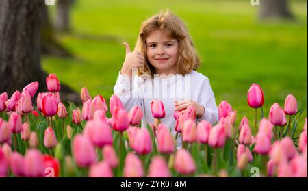 Spannfeder. Kinderspiel im Freien in einem schönen Frühlingsgarten. Kindergesicht in Tulpenblüten. Entzückendes kleines Kind im blühenden Tulpengarten auf der wunderschönen Stockfoto