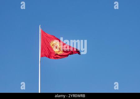 Kirgisistan aktualisierte Flagge flattert gegen den klaren blauen Himmel. Rote neue Flagge der Kirgisischen Republik auf dem Fahnenmast schwenken, echtes Foto. Kirghizia Stockfoto