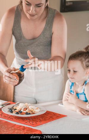 Ein Nahbild einer Mutter am Weihnachtsmorgen, die ihrer Tochter Weihnachtspfannkuchen mit Obst, Sahne und Sirup serviert. Stockfoto