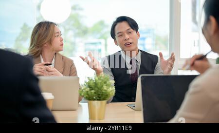 Ein professioneller, intelligenter asiatischer Geschäftsmann in formellem Anzug teilt seine Ideen selbstbewusst mit und erklärt seinem Team während eines gemeinsamen Unternehmens ein Projekt Stockfoto