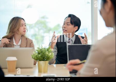 Ein professioneller, intelligenter asiatischer Geschäftsmann in formellem Anzug teilt seine Ideen selbstbewusst mit und erklärt seinem Team während eines gemeinsamen Unternehmens ein Projekt Stockfoto