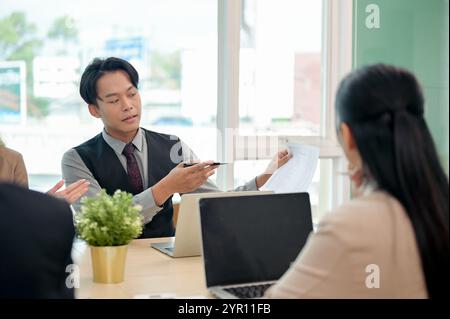 Ein professioneller, intelligenter asiatischer Geschäftsmann in formellem Anzug teilt seine Ideen selbstbewusst mit und erklärt seinem Team während eines gemeinsamen Unternehmens ein Projekt Stockfoto