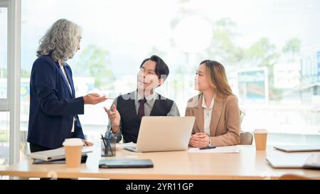 Ein professioneller, intelligenter asiatischer Geschäftsmann in formellem Anzug teilt seine Ideen selbstbewusst mit und erklärt seinem Team während eines gemeinsamen Unternehmens ein Projekt Stockfoto