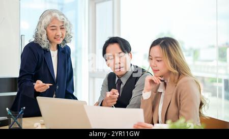 Ein professioneller, intelligenter asiatischer Geschäftsmann in formellem Anzug teilt seine Ideen selbstbewusst mit und erklärt seinem Team während eines gemeinsamen Unternehmens ein Projekt Stockfoto